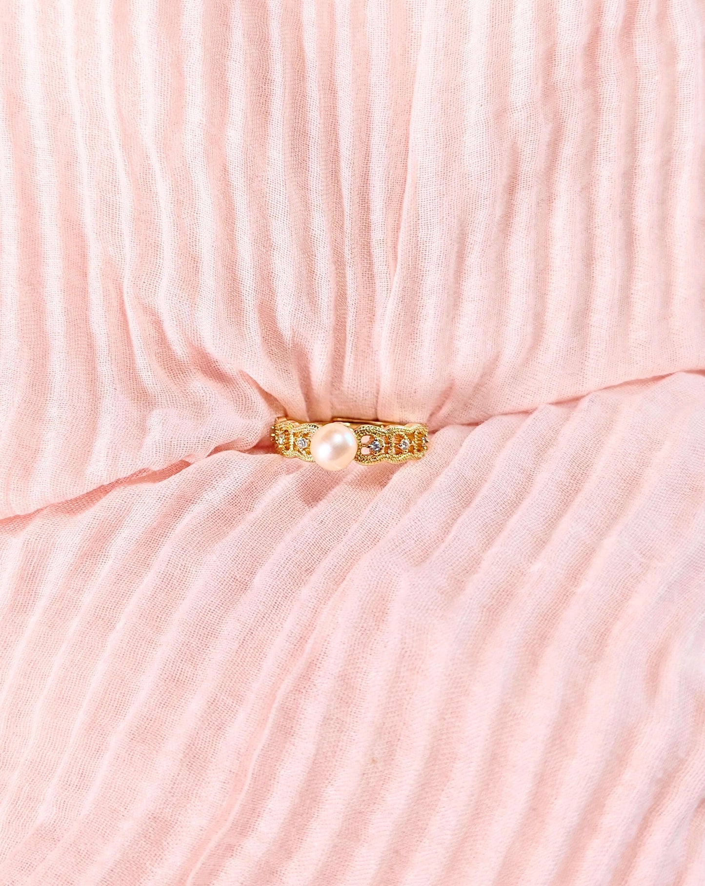 Gold ring with a pearl on a pink textured fabric background