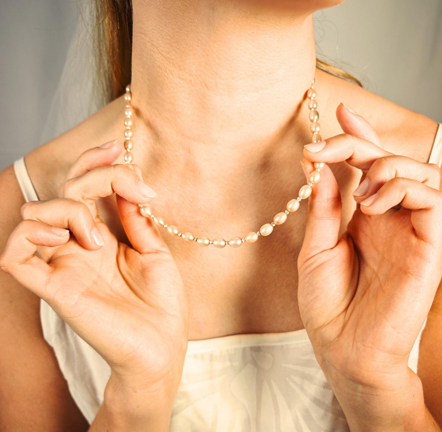 Person wearing a pearl necklace with hands adjusting it