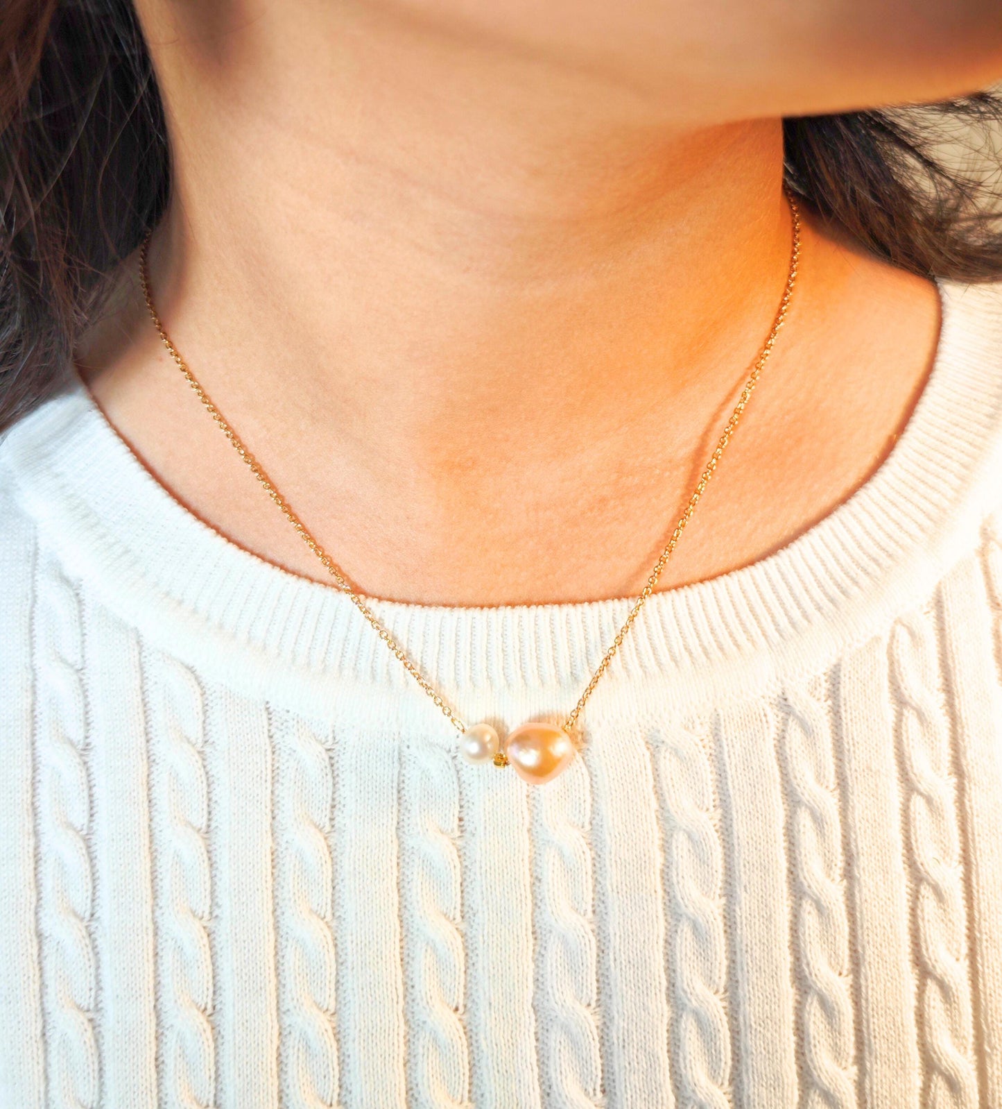 Close-up of a person wearing a gold necklace with a light sweater.