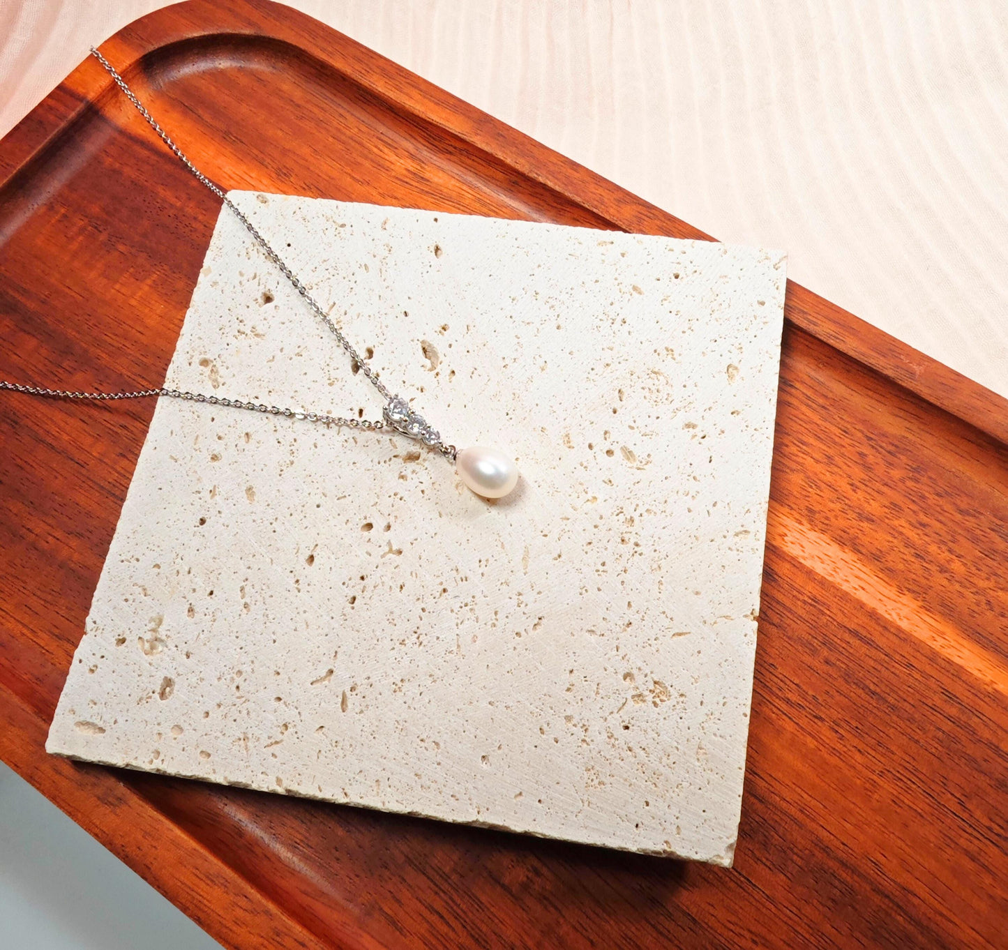 Necklace with a pearl pendant on a textured card, placed on a wooden surface.