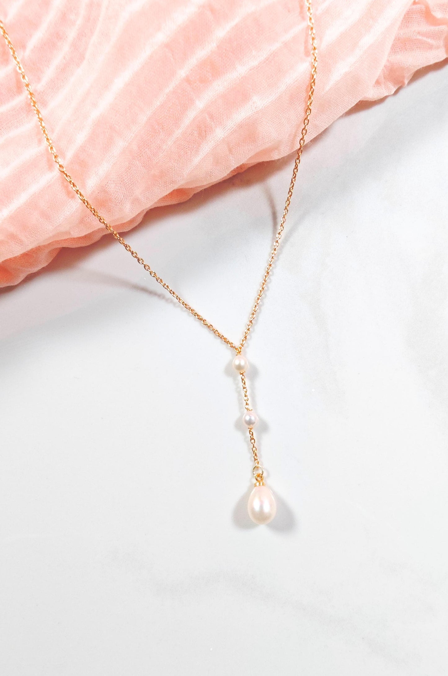 Gold necklace with a pearl pendant on a light pink fabric background