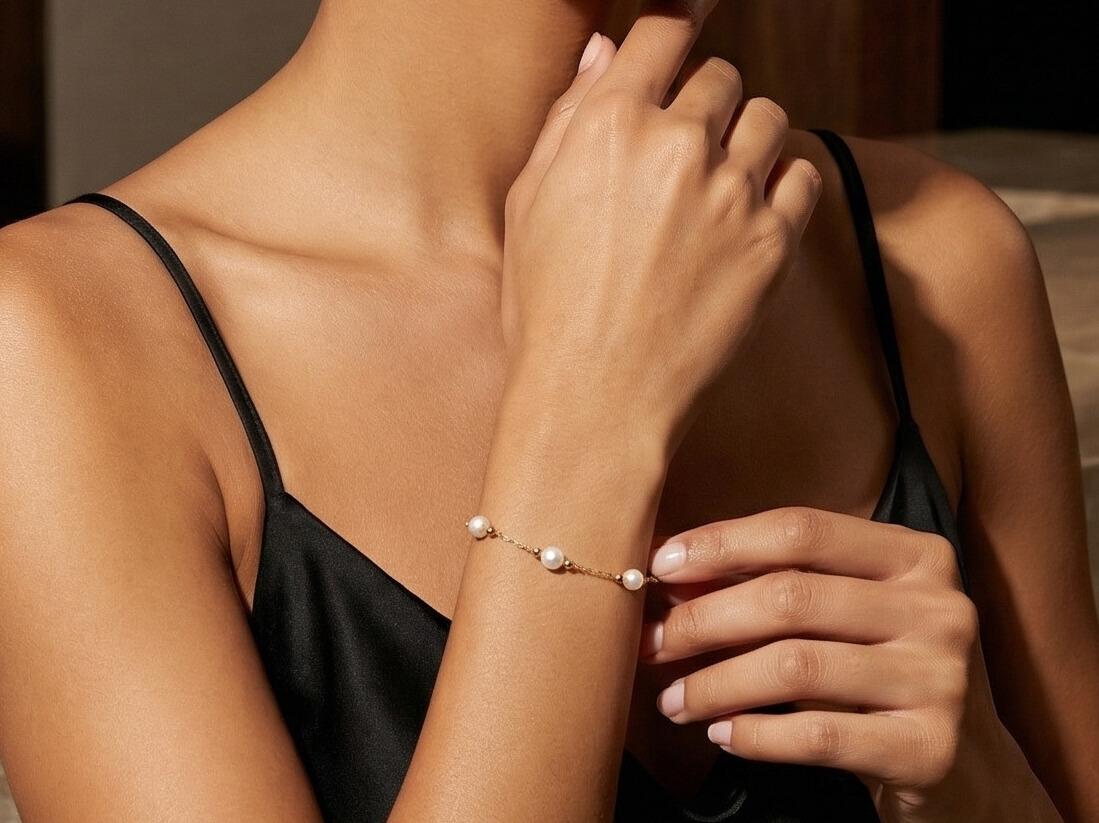 Close-up of a woman's hand wearing a bracelet with pearls, touching her neck.
