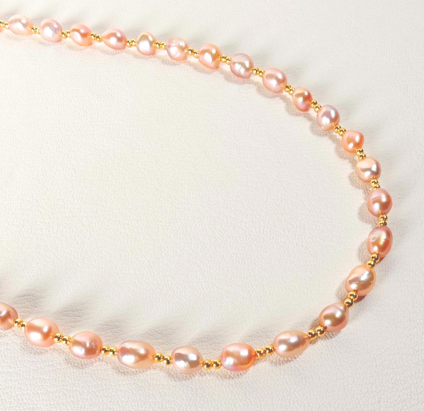 Necklace with pink pearls and gold clasps on a light background