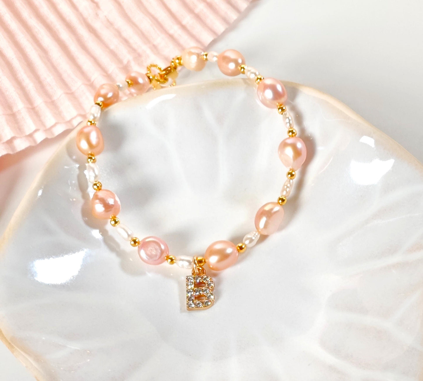Pink pearl bracelet with a gold clasp on a white dish