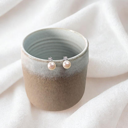 Pearl earrings on a ceramic cup with a soft white background
