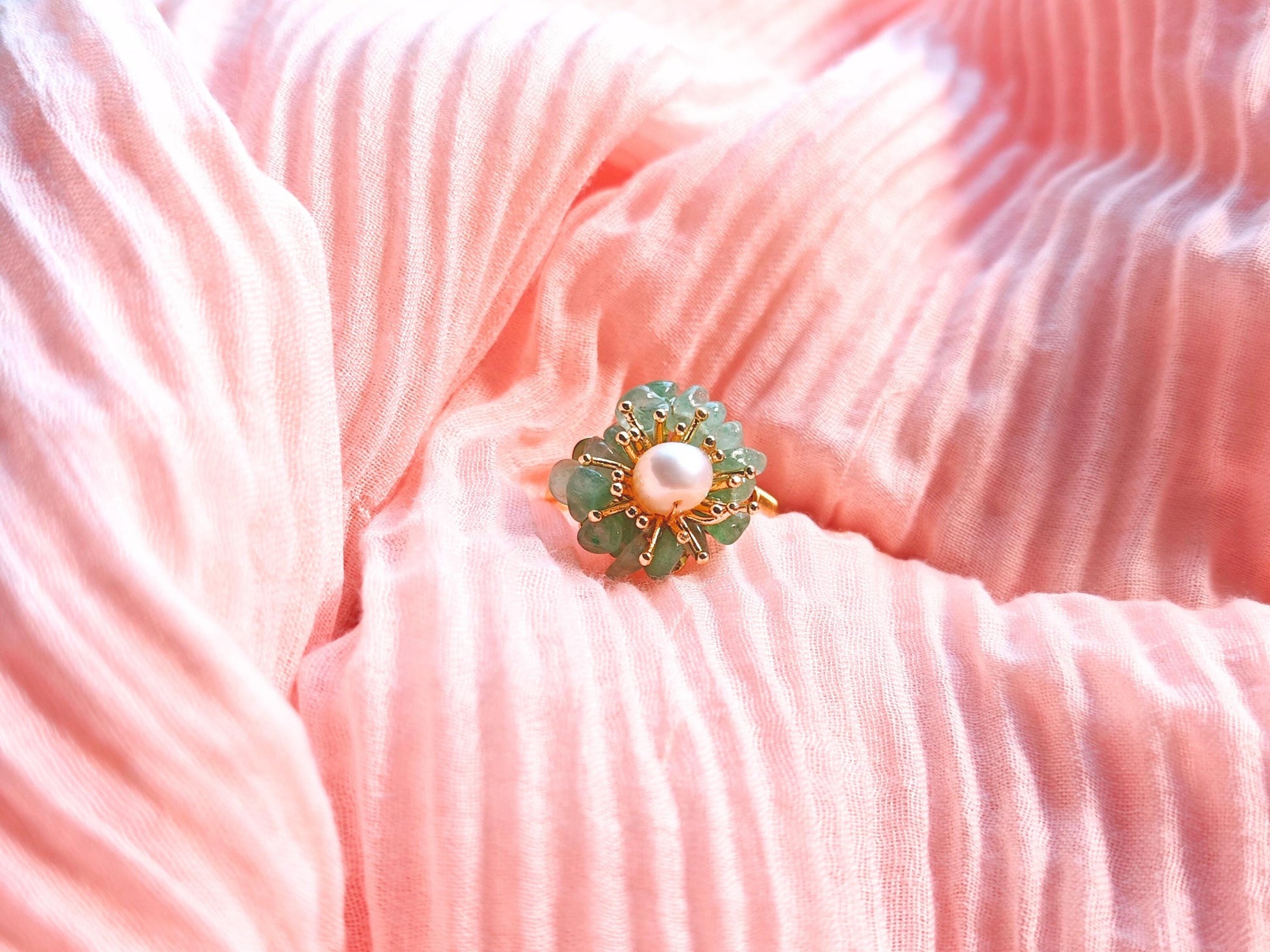 Gold and green brooch with pearl on a pink textured fabric background