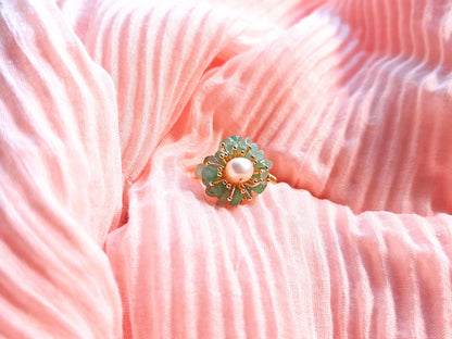 Gold and green brooch with a pearl on a pink textured fabric background