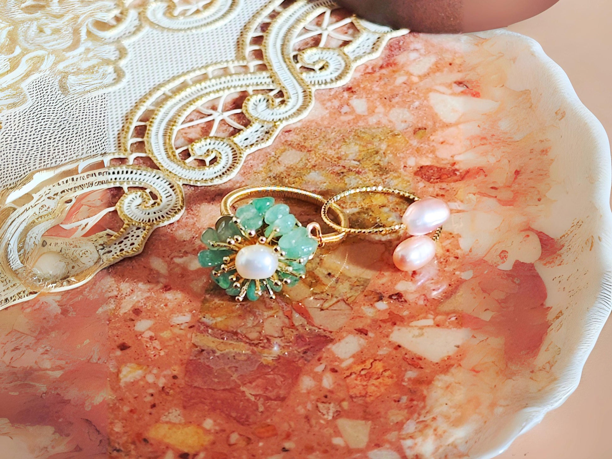 Gold ring with green gemstone and pearl on a textured surface