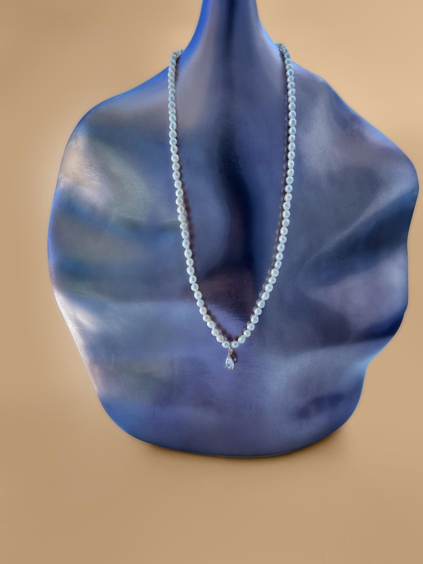 Pearl necklace on a blue mannequin bust against a beige background