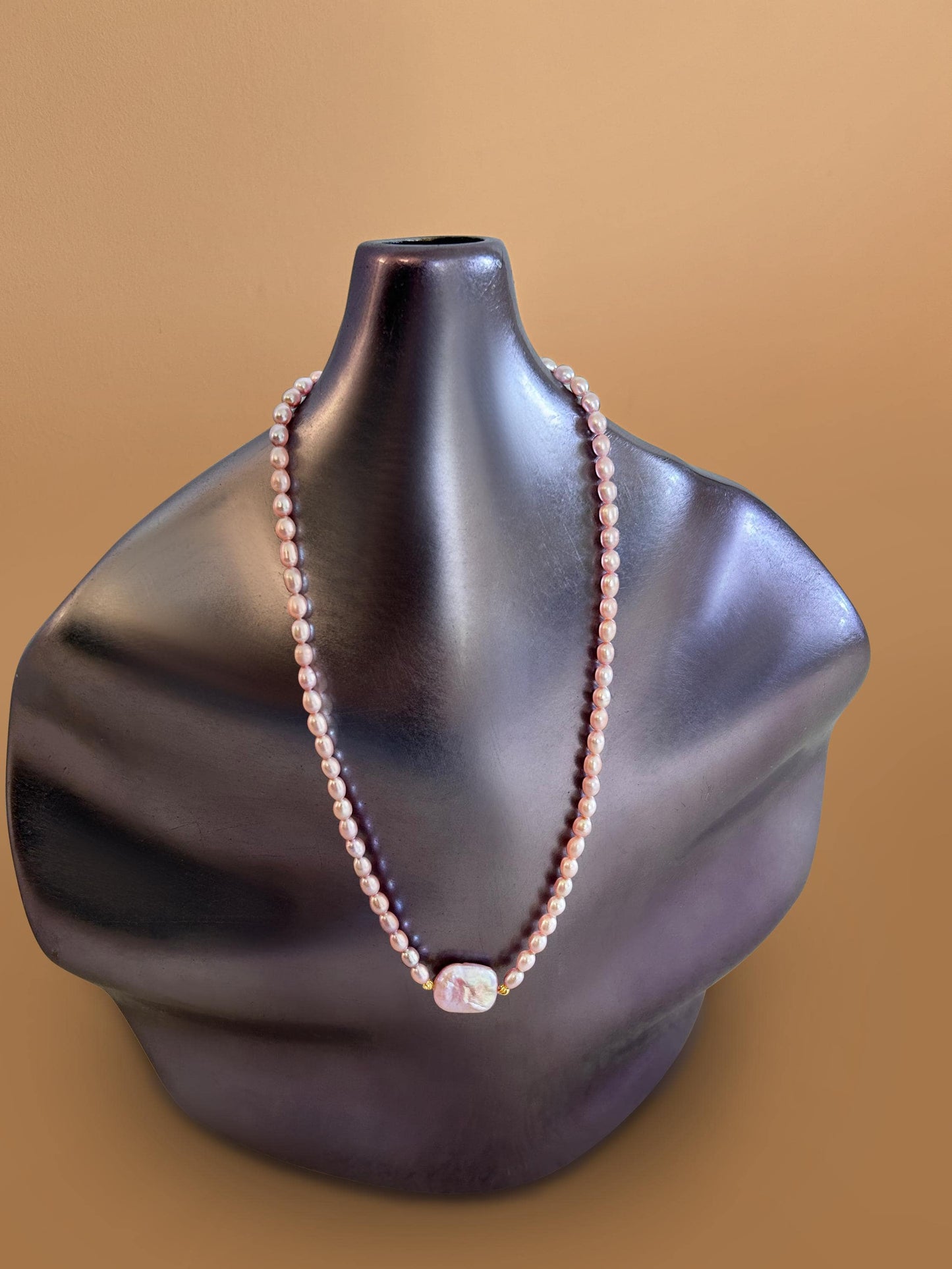 Pearl necklace on a black mannequin bust against a brown background
