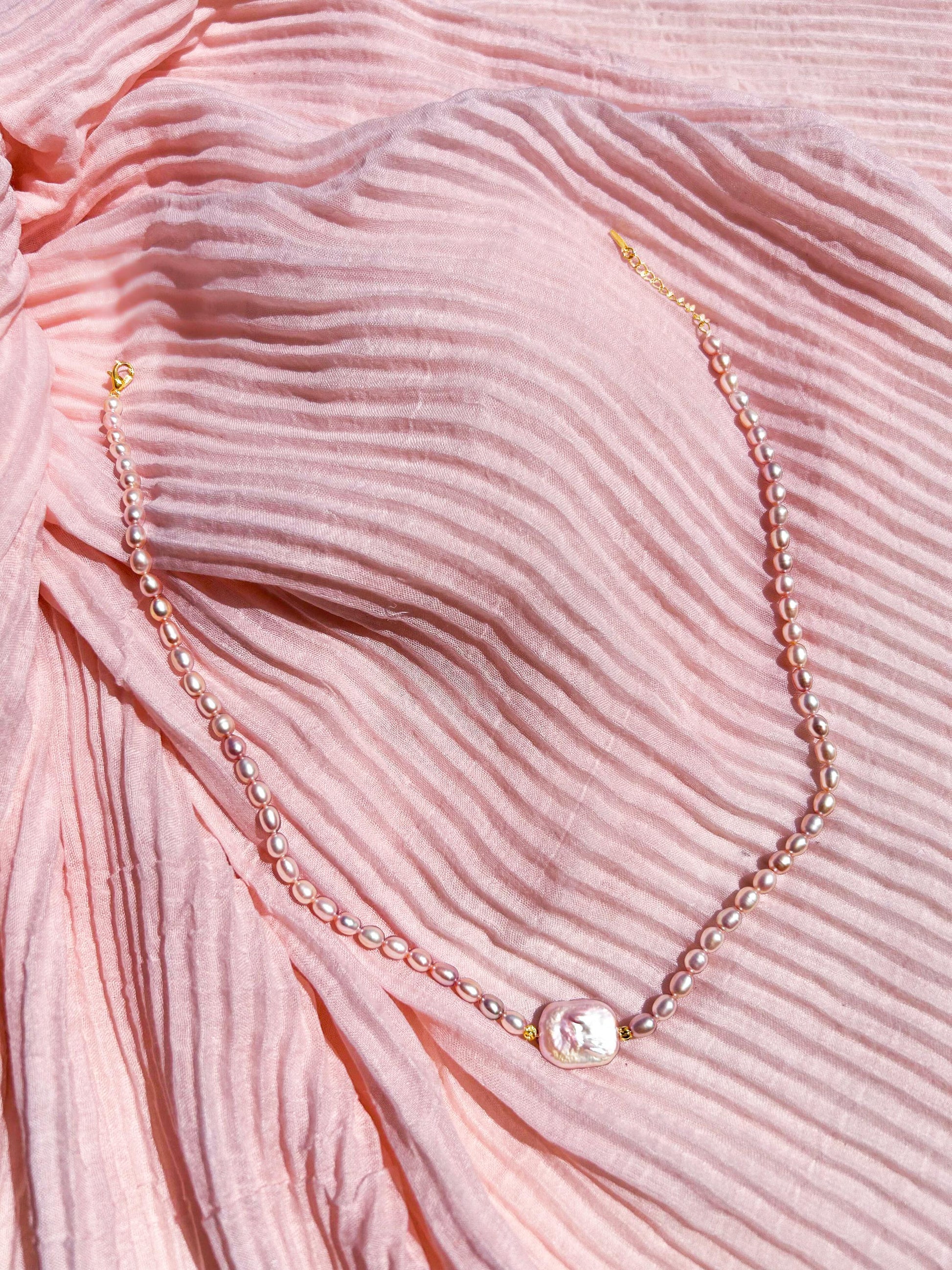 Pearl necklace on a pink textured fabric background