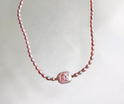Pearl necklace with a large pink pearl on a light background
