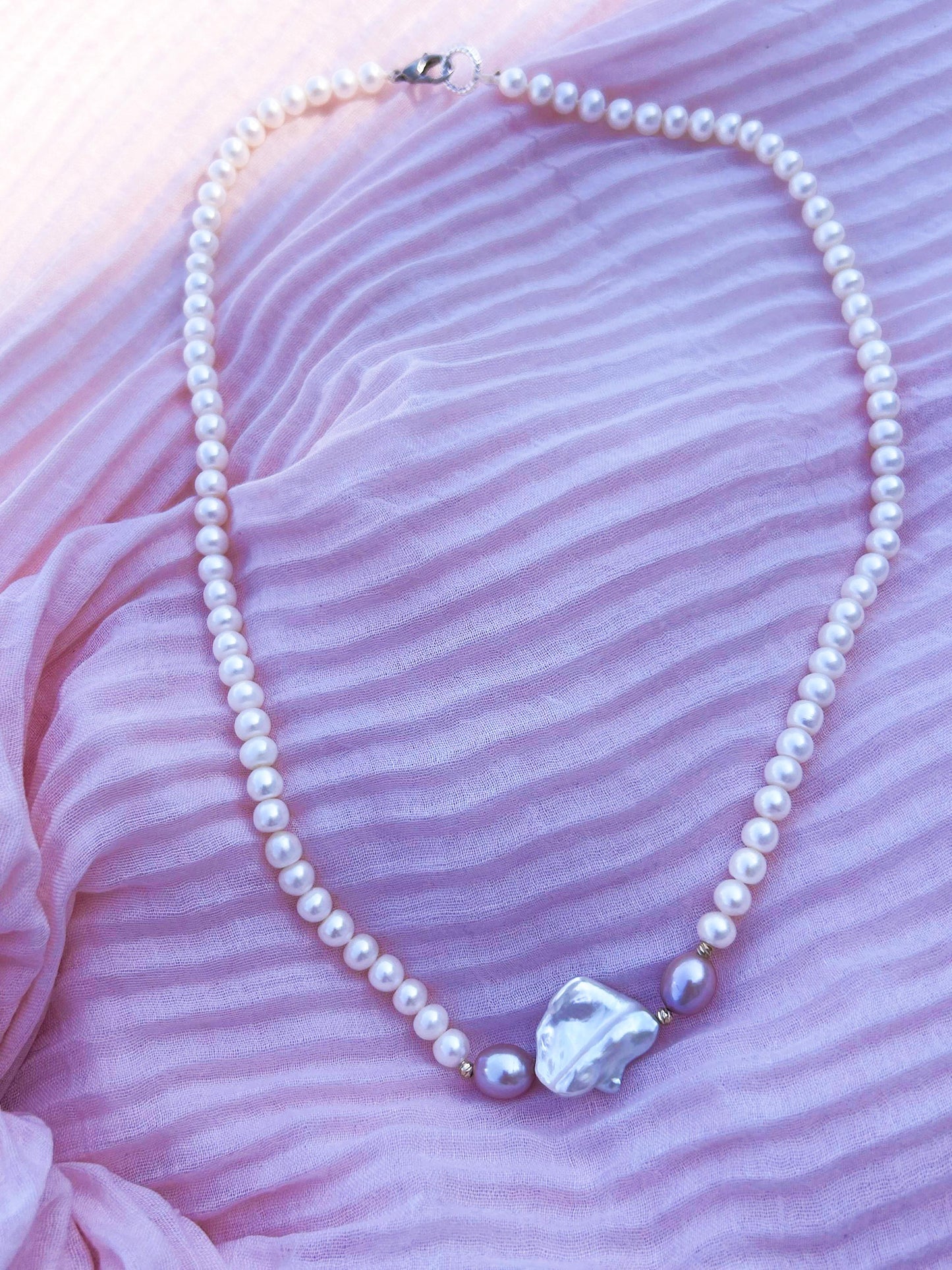 Pearl necklace with a large pearl pendant on a pink fabric background