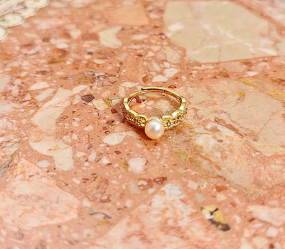 Gold ring with a pearl on a textured pink surface