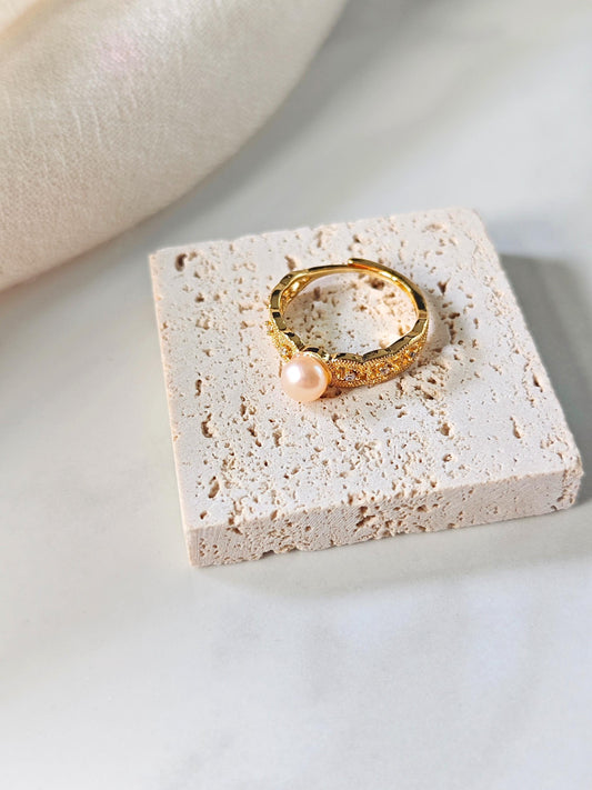 Gold ring with a pearl on a textured white surface