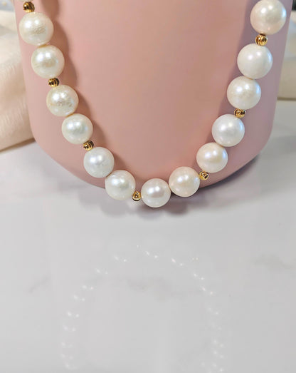 Pearl necklace with gold beads on a pink stand against a white background