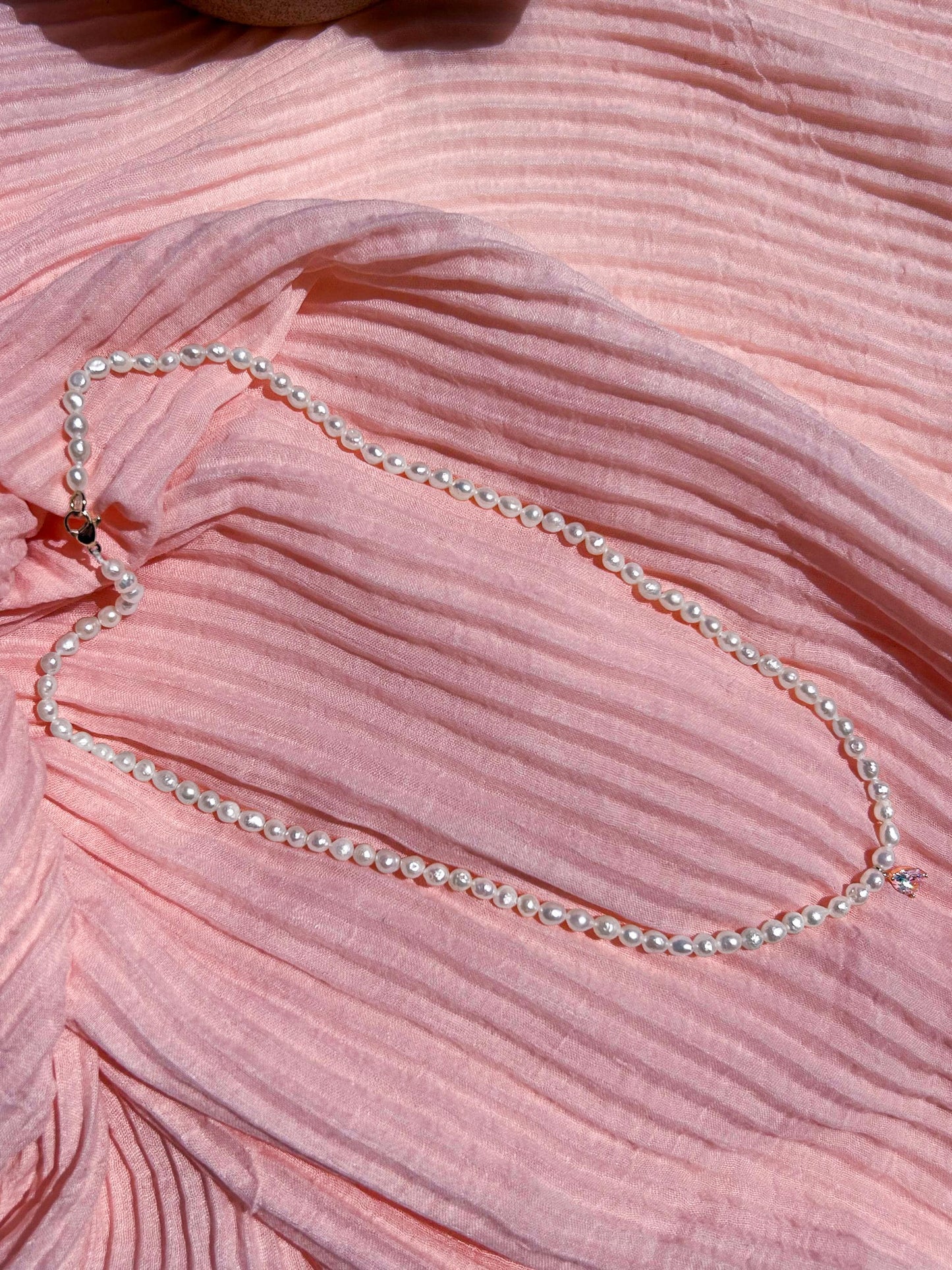 Pearl necklace on a pink textured fabric background