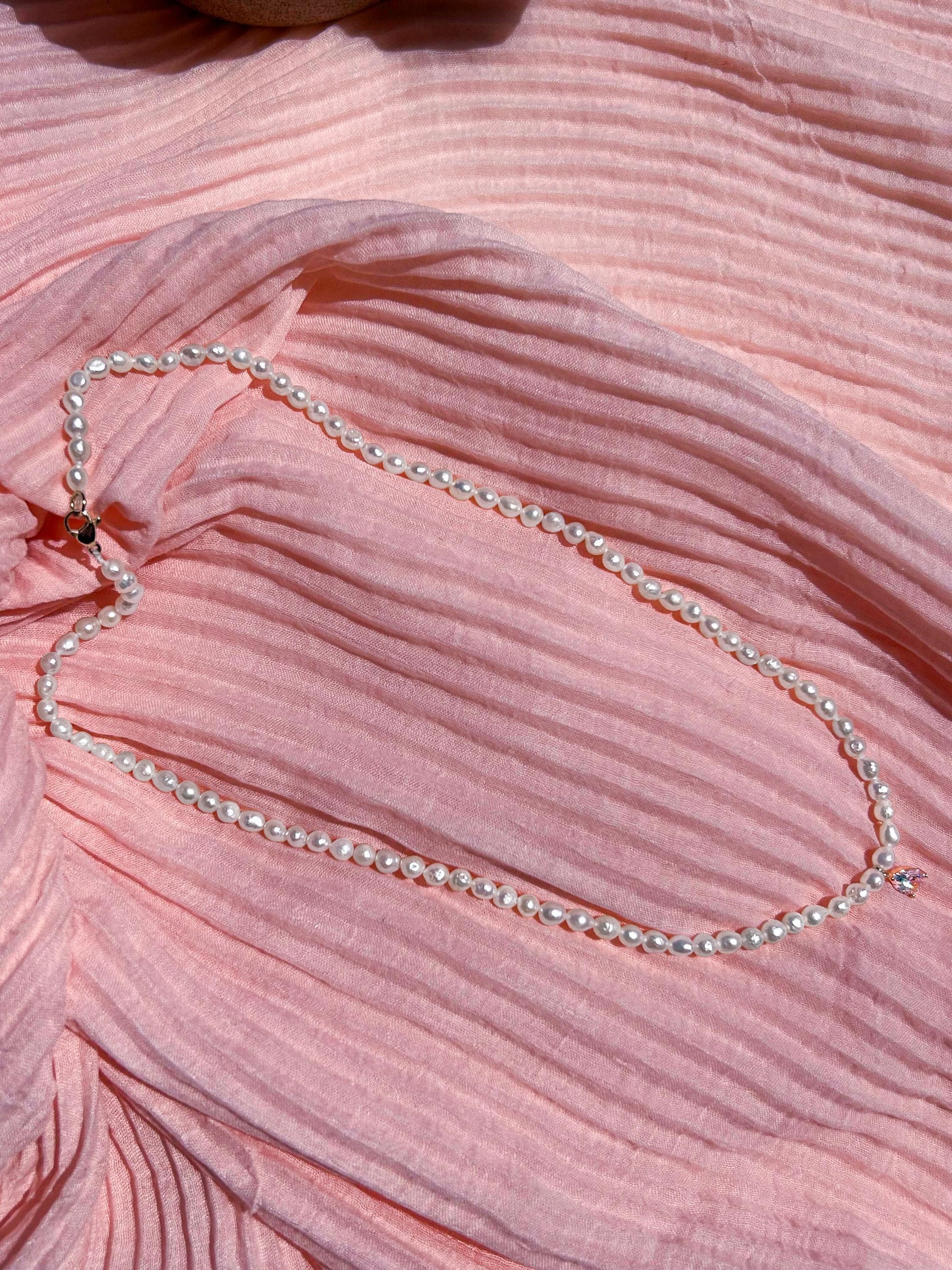 Pearl necklace on a pink textured fabric background