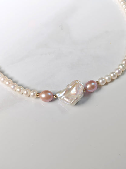 Pearl necklace with a large baroque pearl on a light gray background