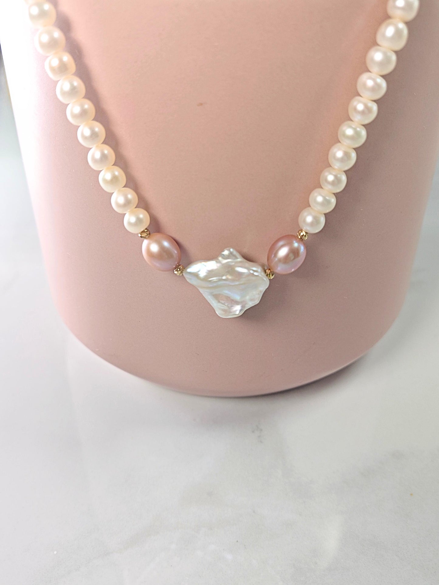 Pearl necklace with a large central gemstone on a pink stand.