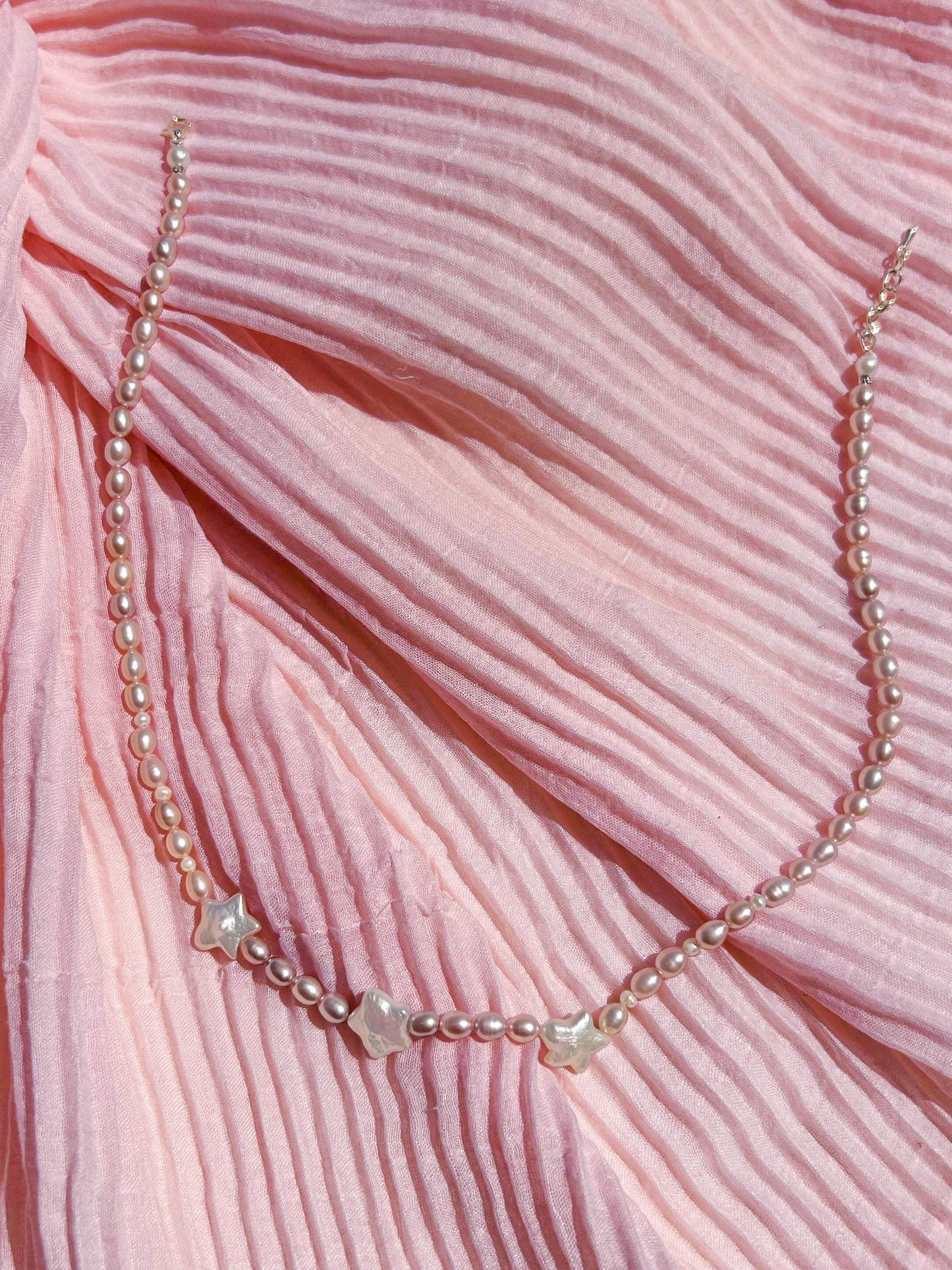 Pearl necklace with star-shaped beads on a pink textured fabric background