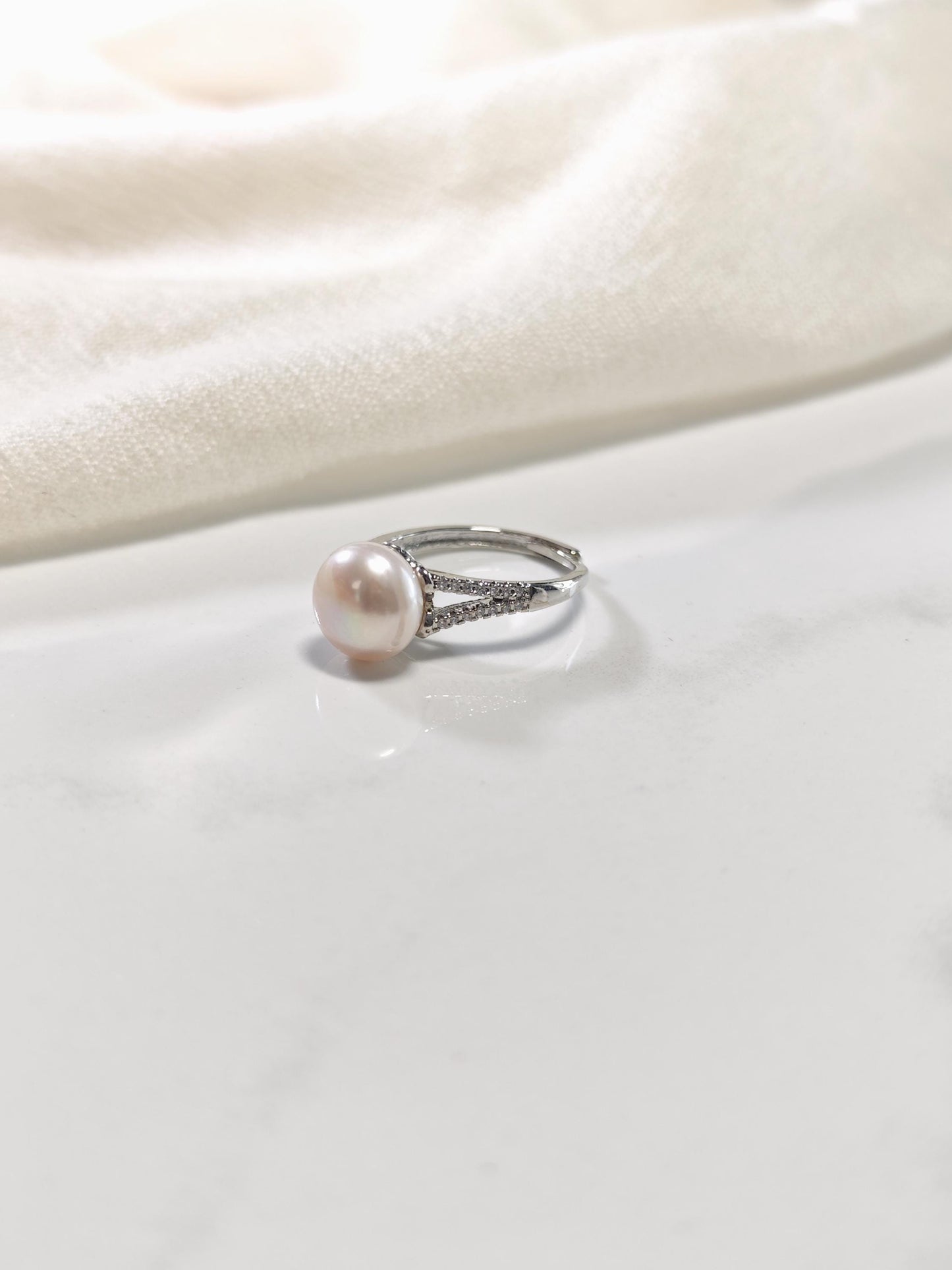 Pearl ring with silver band on a white fabric background