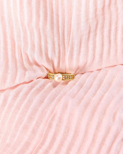 Gold ring with a pearl on a pink textured fabric background