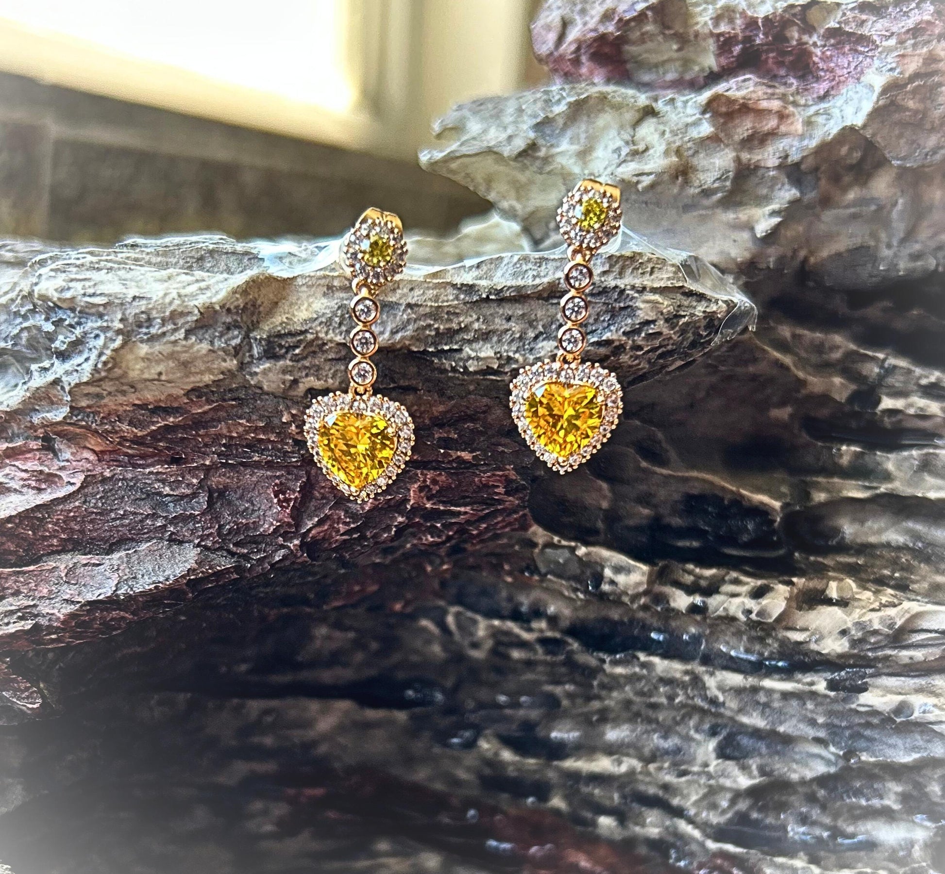 Heart-shaped yellow gemstone earrings on a textured stone surface