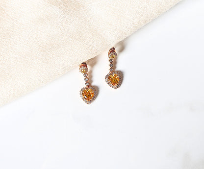 Pair of heart-shaped earrings with orange gemstones on a light background