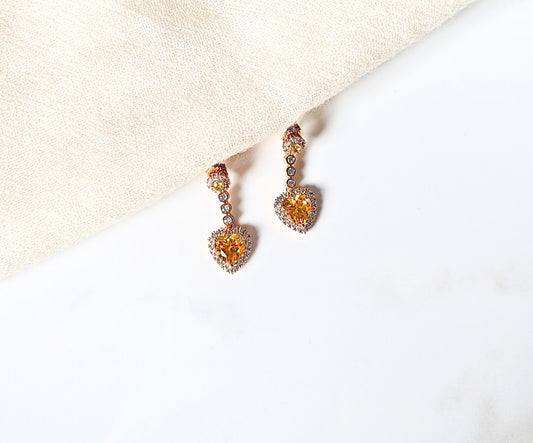 Pair of heart-shaped earrings with orange gemstones on a light background