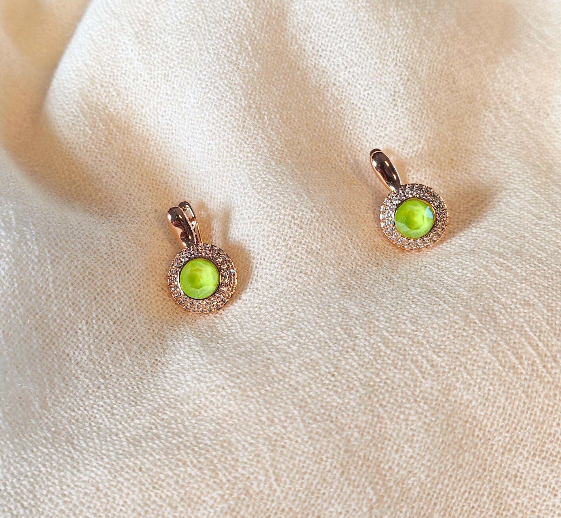 Pair of earrings with green gemstones on a beige fabric background
