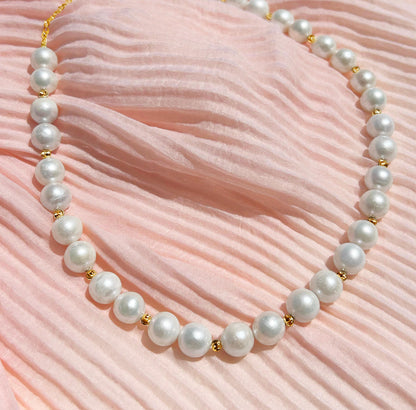 Pearl necklace with gold accents on a pink textured fabric background