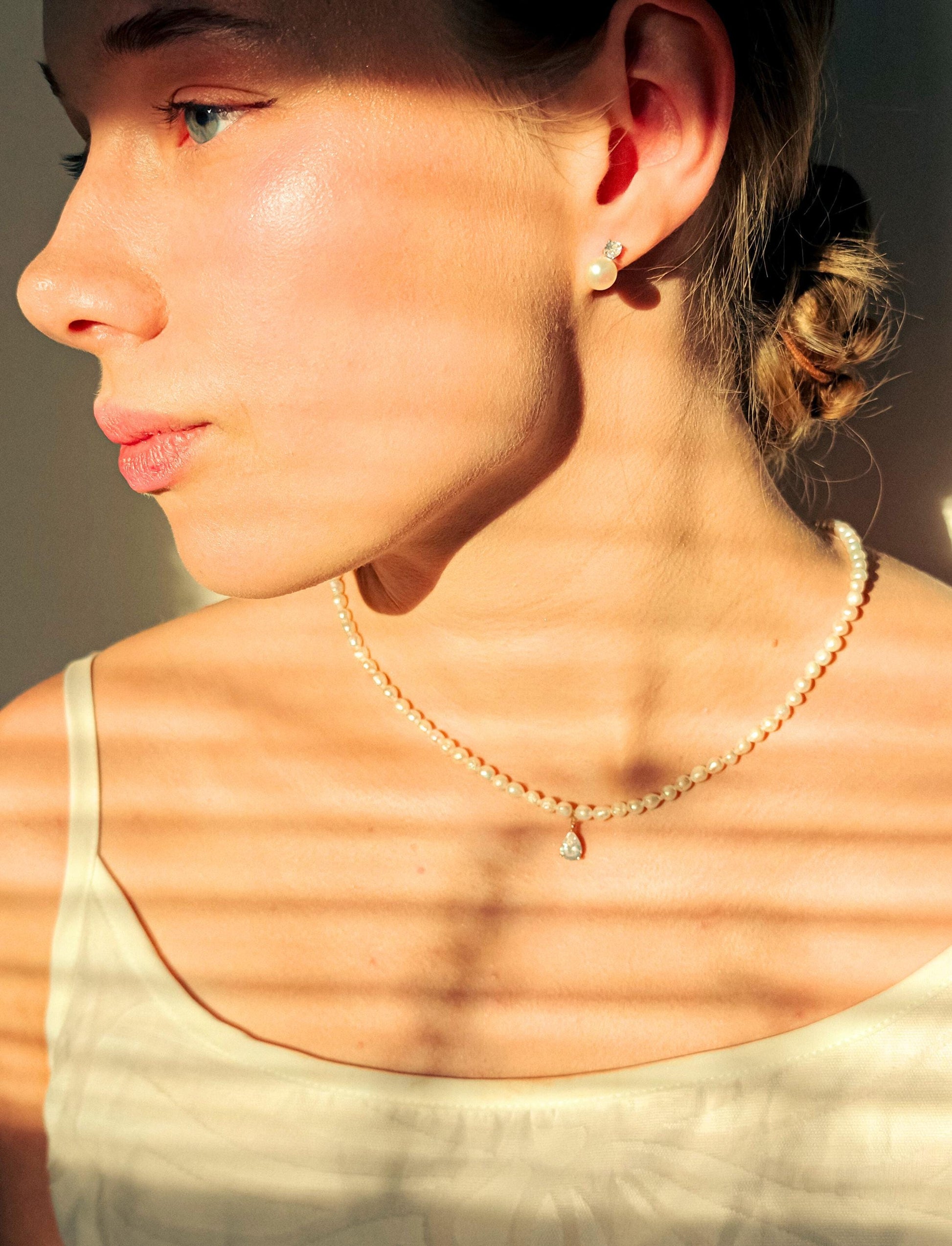 Woman wearing a pearl necklace with sunlight casting shadows on her skin