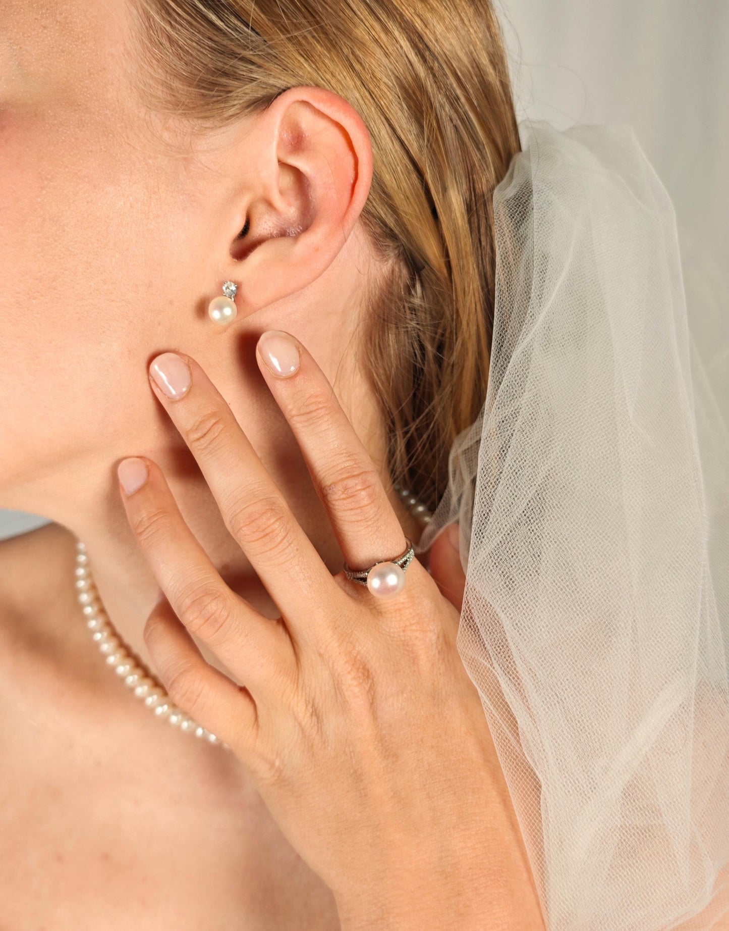 Close-up of a person wearing pearl earrings and a ring, with a blurred background.