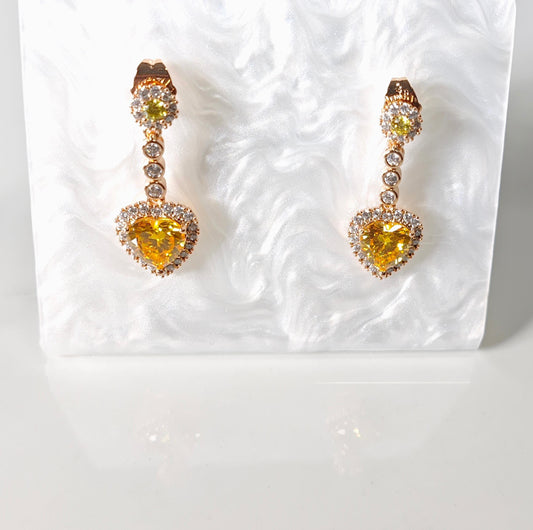Pair of yellow heart-shaped gemstone earrings on a textured white background