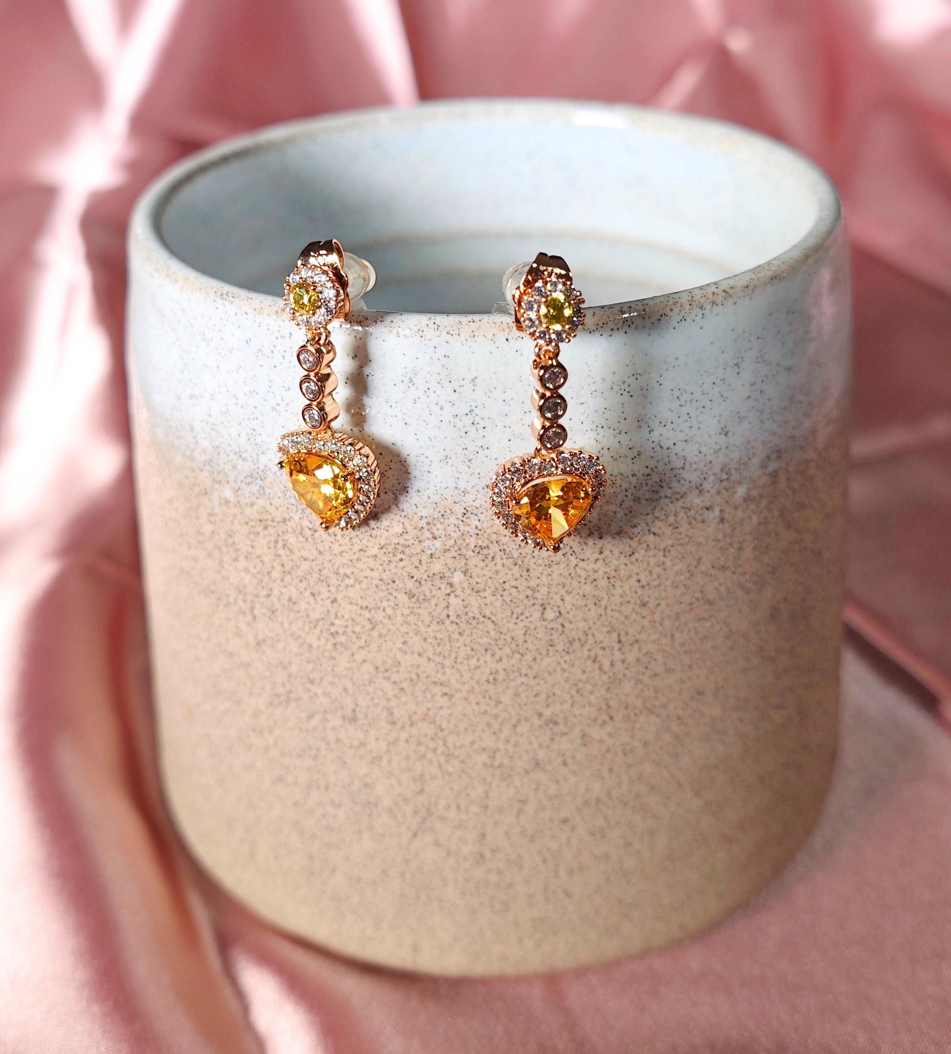 Pair of earrings with heart-shaped gemstones in a ceramic holder on a pink background