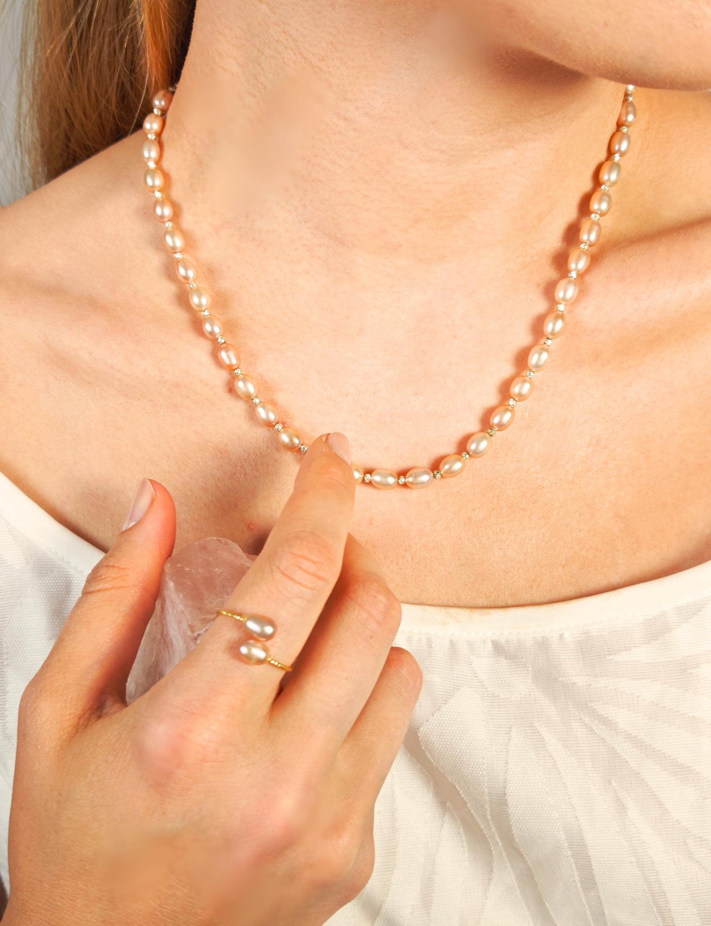 Pearl necklace being adjusted by a hand with a ring on a light background