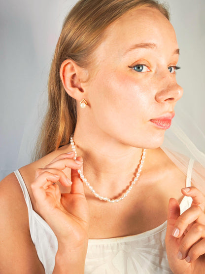 Woman wearing a pearl necklace and earrings against a neutral background