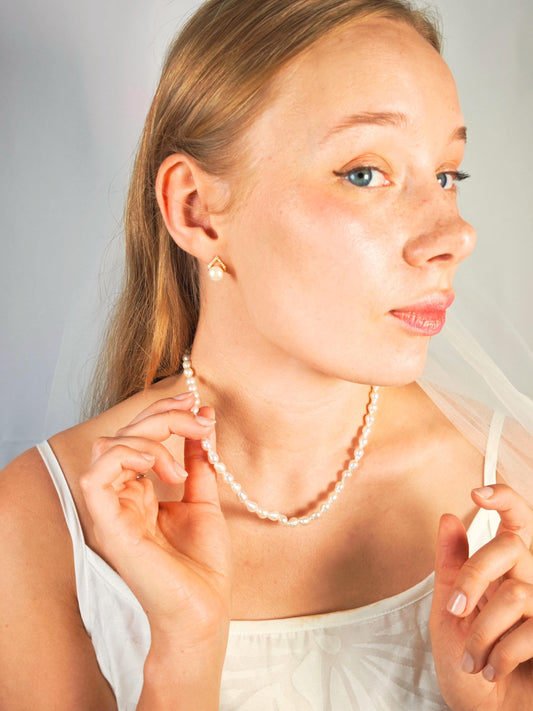 Woman wearing a pearl necklace and earrings against a neutral background