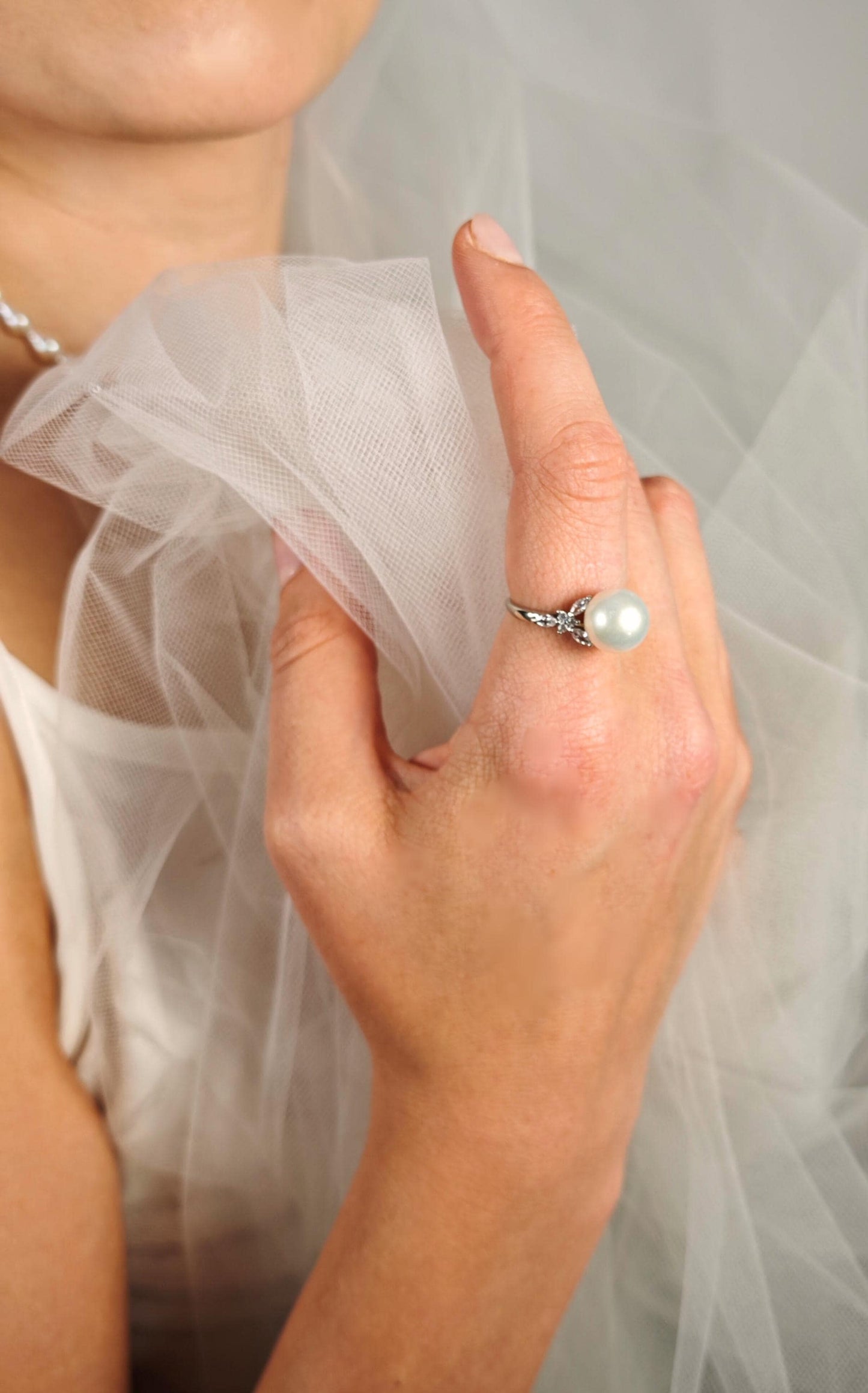 Close-up of a hand wearing a pearl ring with a blurred background