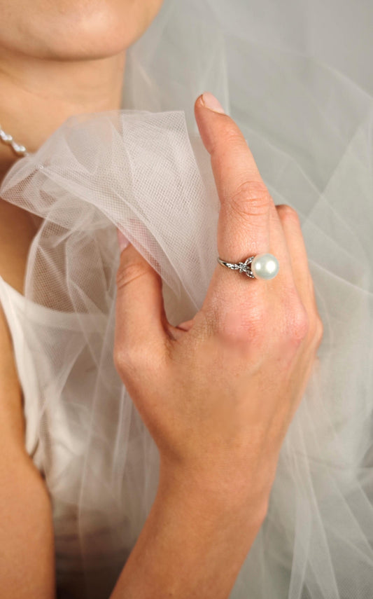 Close-up of a hand wearing a pearl ring with a blurred background