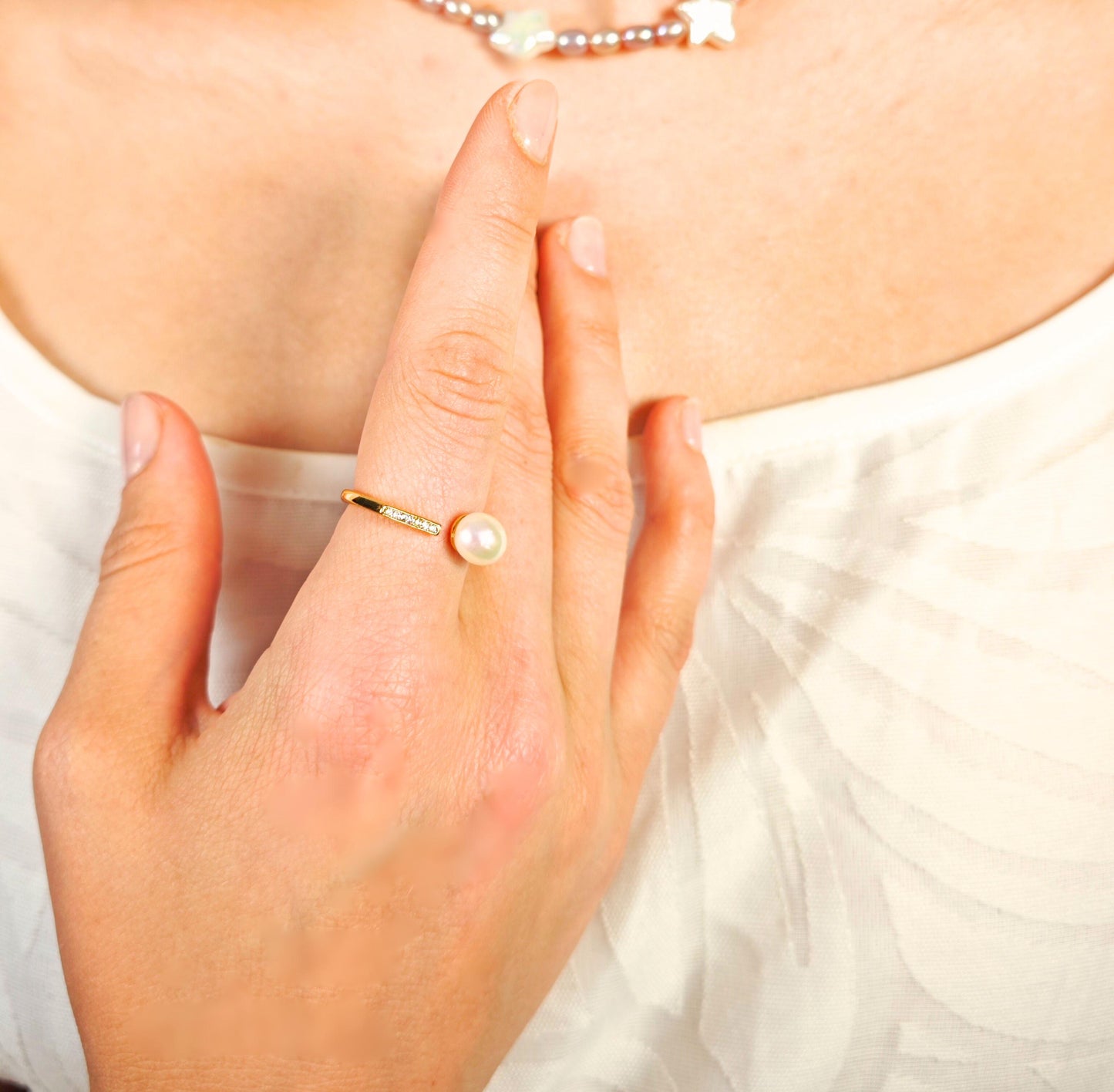 Close-up of a hand wearing a gold ring with a pearl on a white background