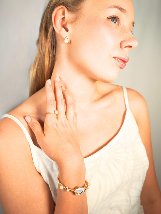 Woman wearing gold jewelry including earrings, ring, and bracelet against a neutral background