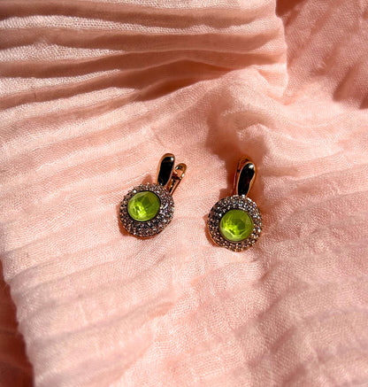 Pair of earrings with green gemstones on a pink fabric background