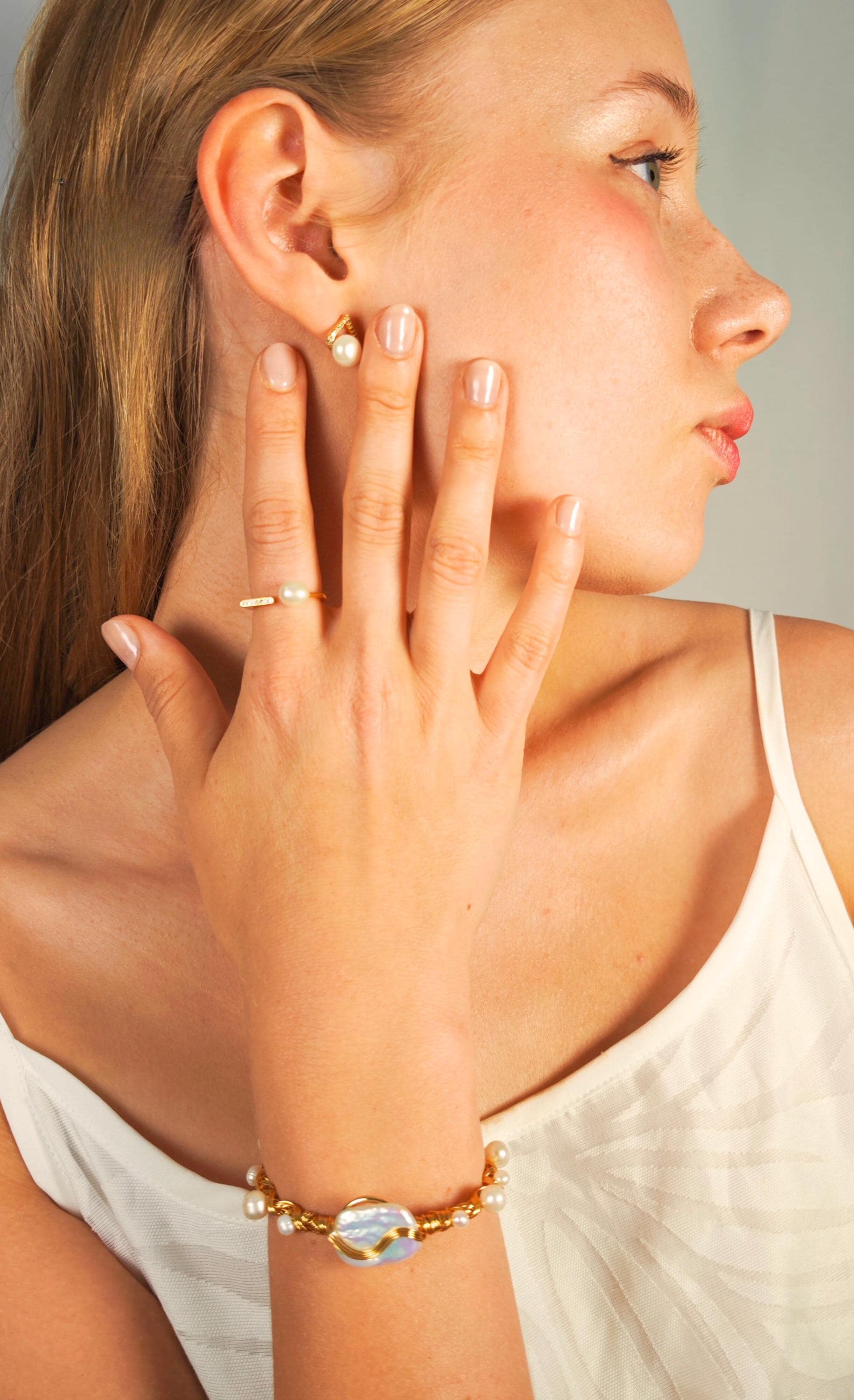 Woman wearing a pearl earring and gold bracelet, close-up of face and hand.