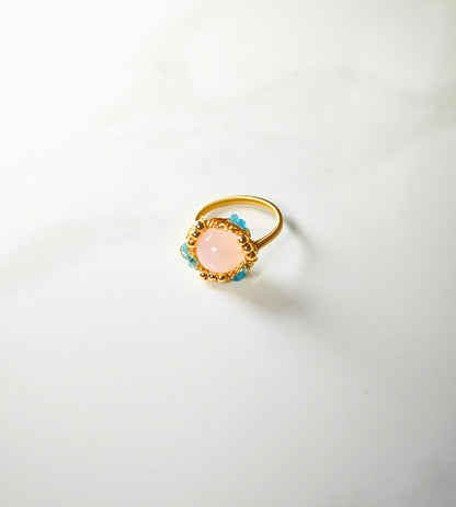 Gold ring with a pink gemstone and blue accents on a white background