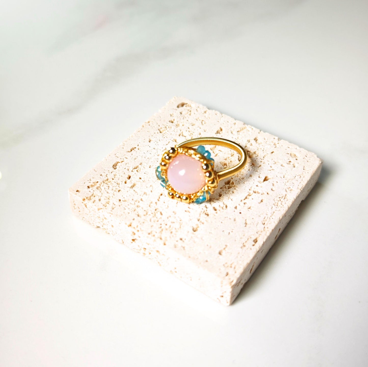 Gold ring with a pink gemstone on a textured white stand