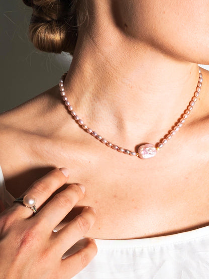 Close-up of a person wearing a pearl necklace with a hand holding a ring.