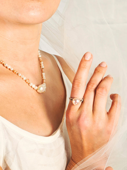 Pearl necklace and ring on a person against a light background