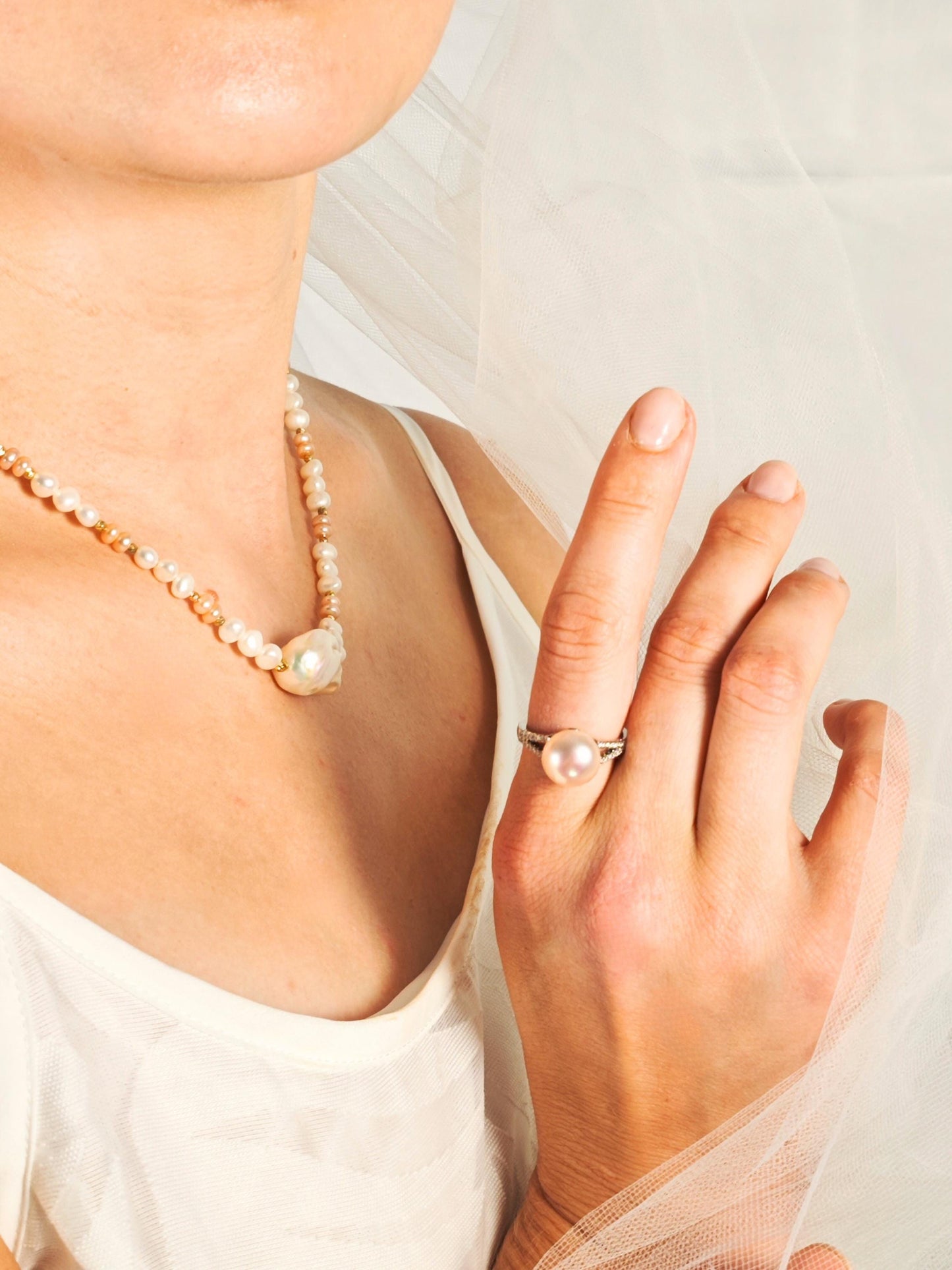 Pearl necklace and ring on a person against a light background
